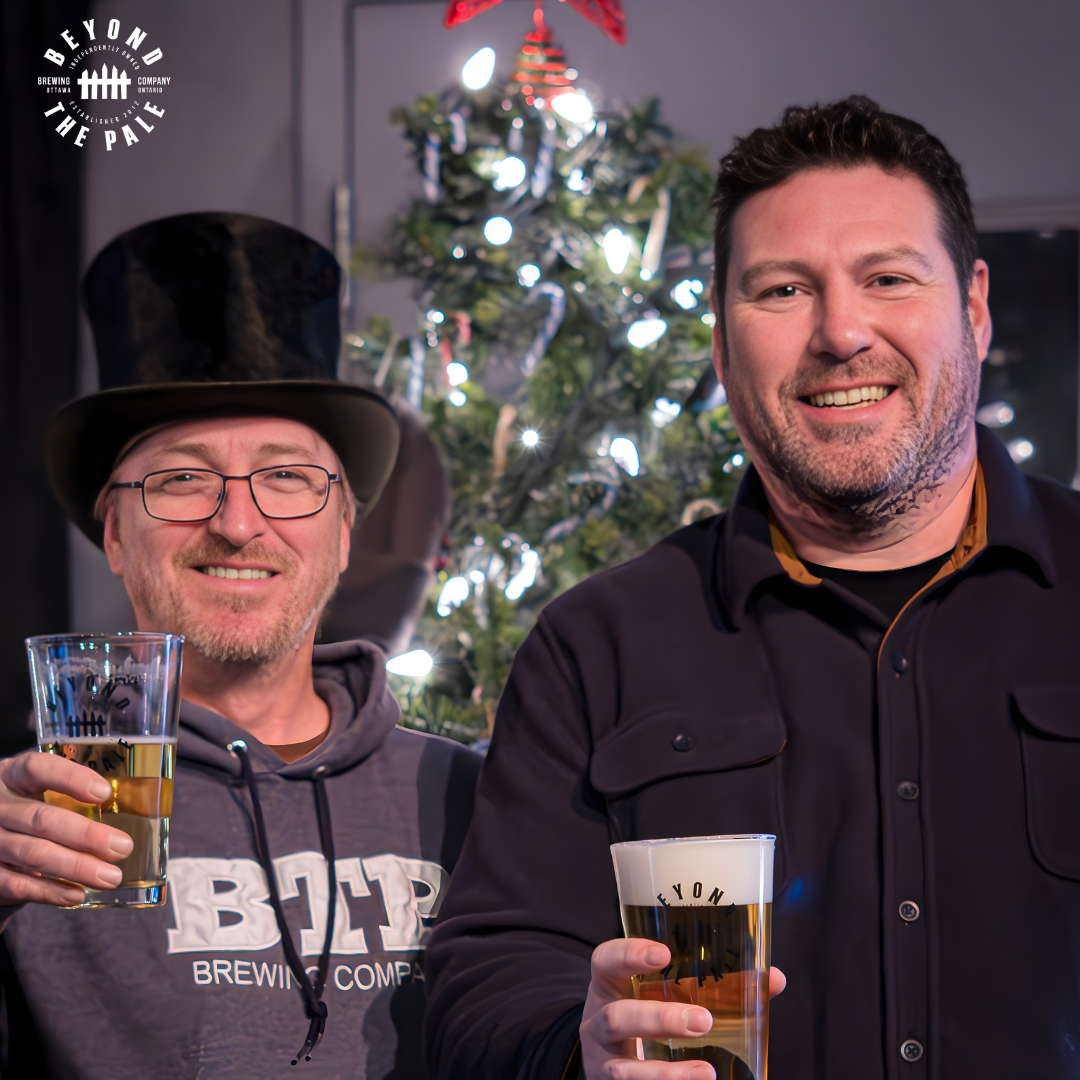 Two men holding beer glasses in front of a Christmas tree, with 'Beyond the Pale Brewing Company' branding.